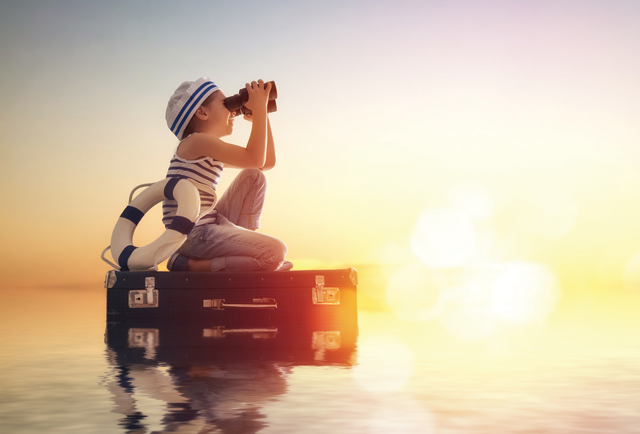 boy dressed in sailor outfit looking out to sea with binoculars